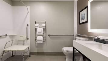 A modern bathroom with a white toilet, a sink with a mirror, a towel rack, and a wheelchair-accessible chair.