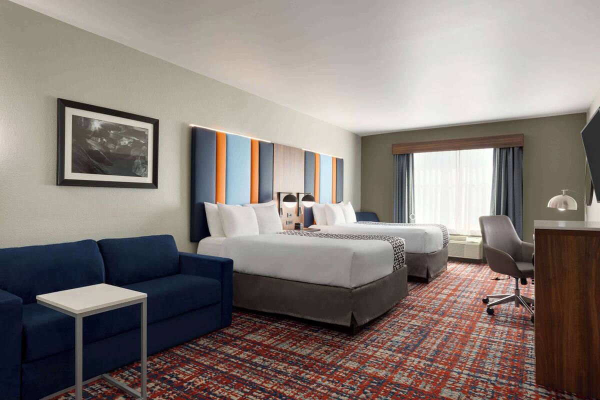 Une chambre d’hôtel avec deux lits, un canapé bleu, une petite table, un bureau et une moquette à motifs.