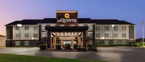 A La Quinta hotel with a modern design, featuring a prominent entrance with a sun logo, multiple windows, and a well-maintained lawn.