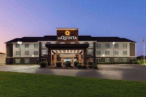 Hotel La Quinta con diseño moderno, destacando una entrada con el logo del sol, múltiples ventanales y un césped bien cuidado.