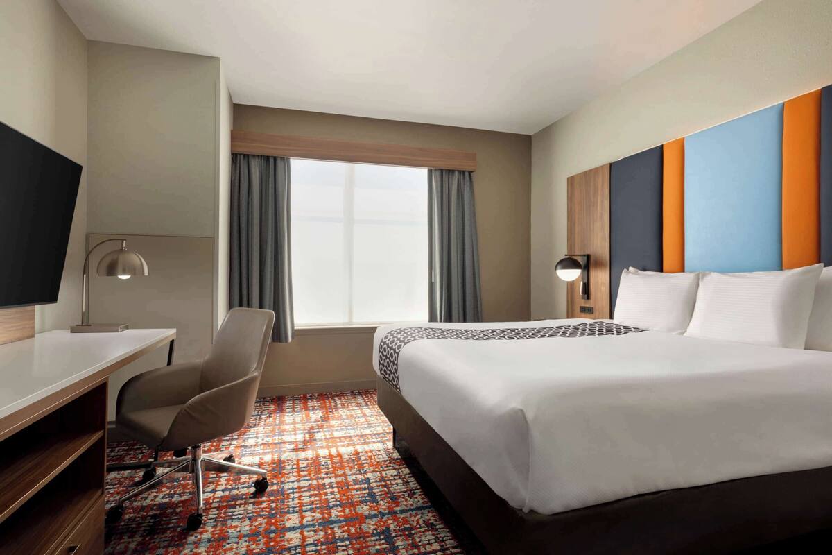 Une chambre d’hôtel avec un grand lit, un bureau avec une chaise, une télévision et une fenêtre avec des rideaux.