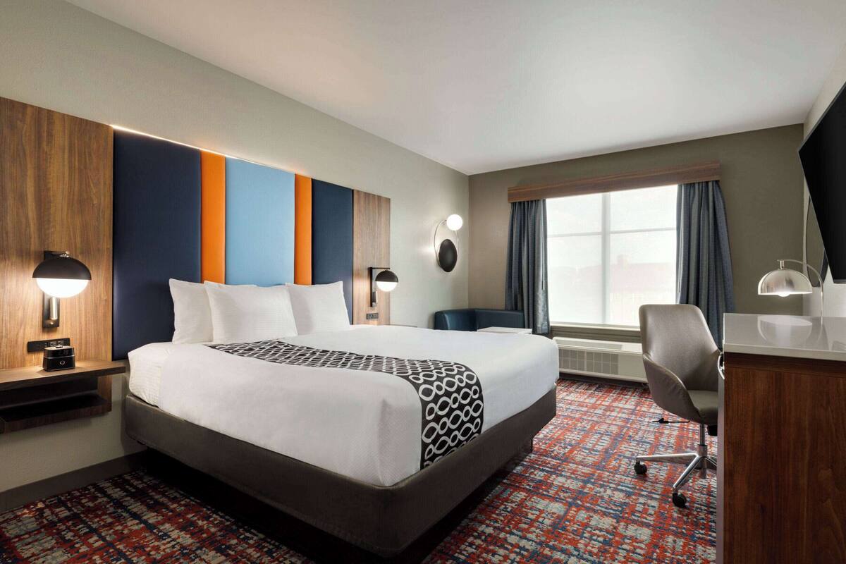 Une chambre d’hôtel avec un grand lit, un bureau, une chaise, une lampe de bureau, un téléviseur fixé au mur et une fenêtre avec des rideaux.