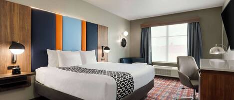 A hotel room with a large bed, a desk, a chair, a desk lamp, a wall-mounted TV, and a window with curtains.