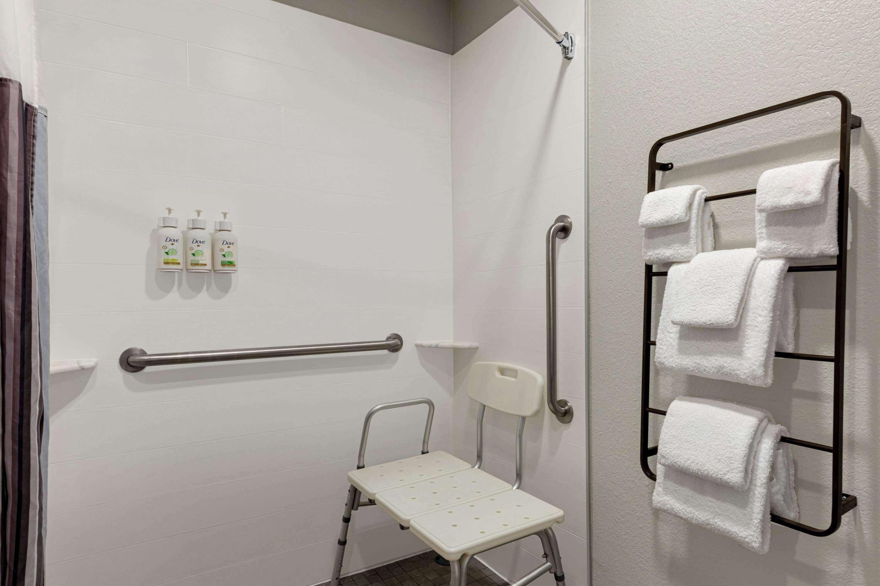 A bathroom with a shower, grab bars, a wheelchair-accessible bench, and a towel rack.