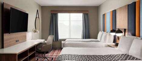 A hotel room with two beds, a desk, a TV, and a window with curtains.