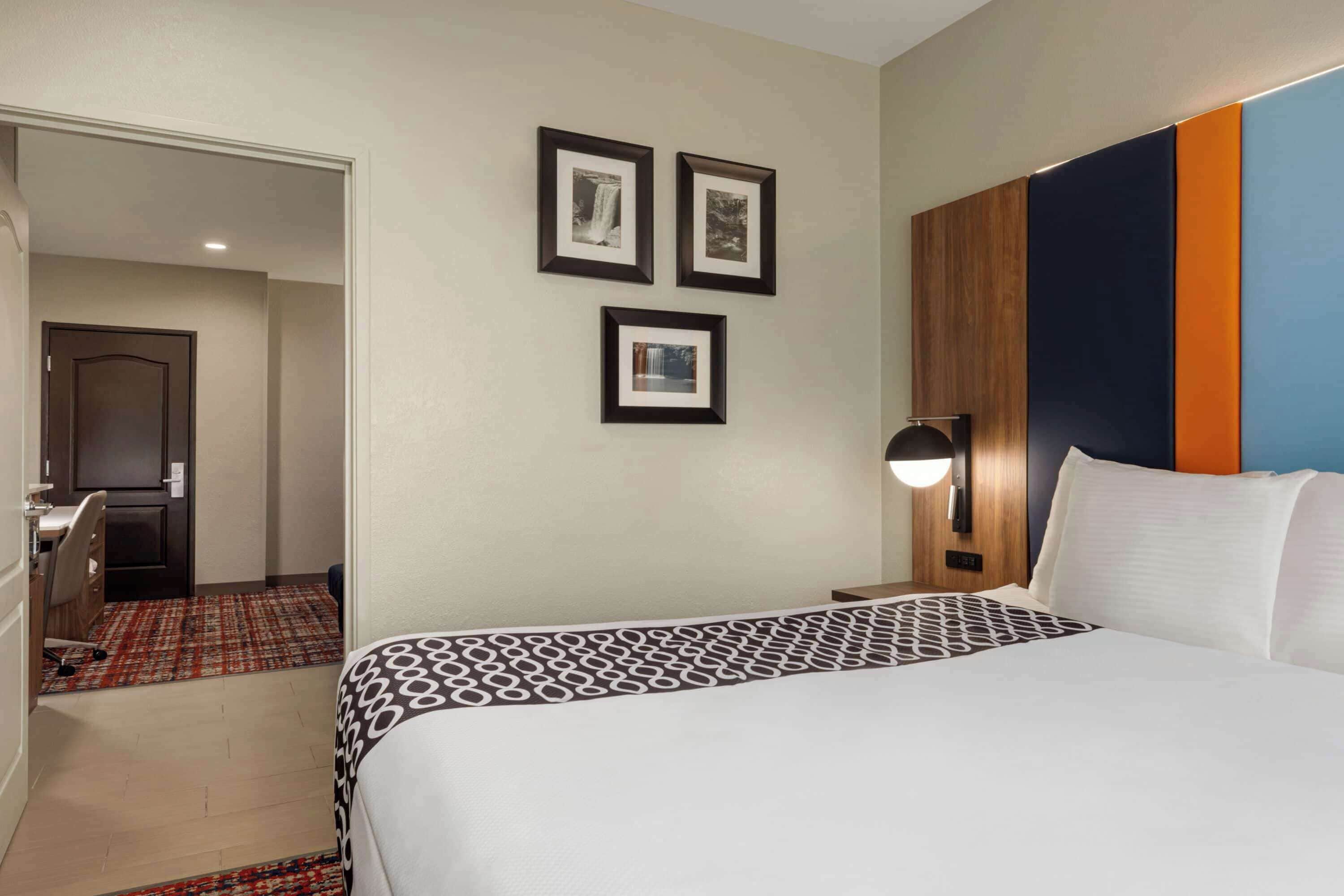 A hotel room with a bed, a desk, and a chair. There are three framed pictures on the wall.