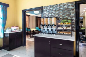 Een hotelkamer met een kitchenette voorzien van een yoghurtdispenser, een koffieapparaat en een selectie gebak.