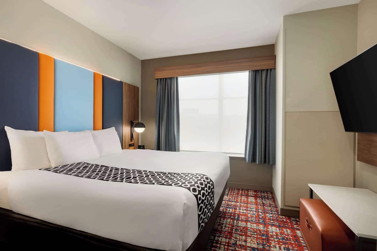 Une chambre d’hôtel avec un grand lit, un bureau, une télévision et une fenêtre avec des rideaux.
