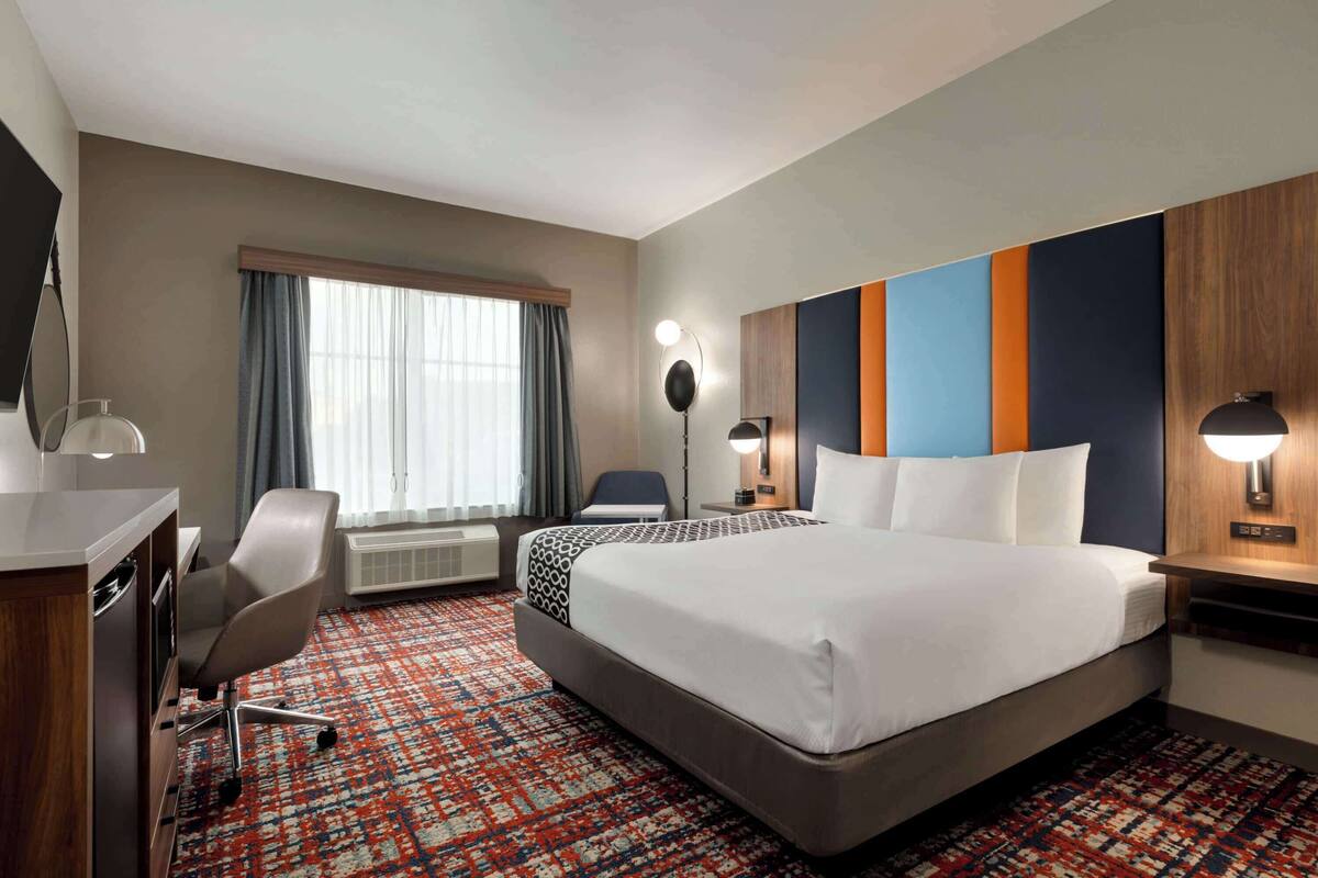Une chambre d’hôtel avec un grand lit, un bureau avec une chaise, une télévision et une fenêtre avec des rideaux.