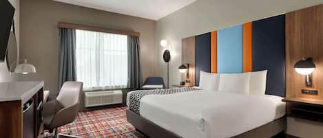 A hotel room with a large bed, a desk with a chair, a TV, and a window with curtains.