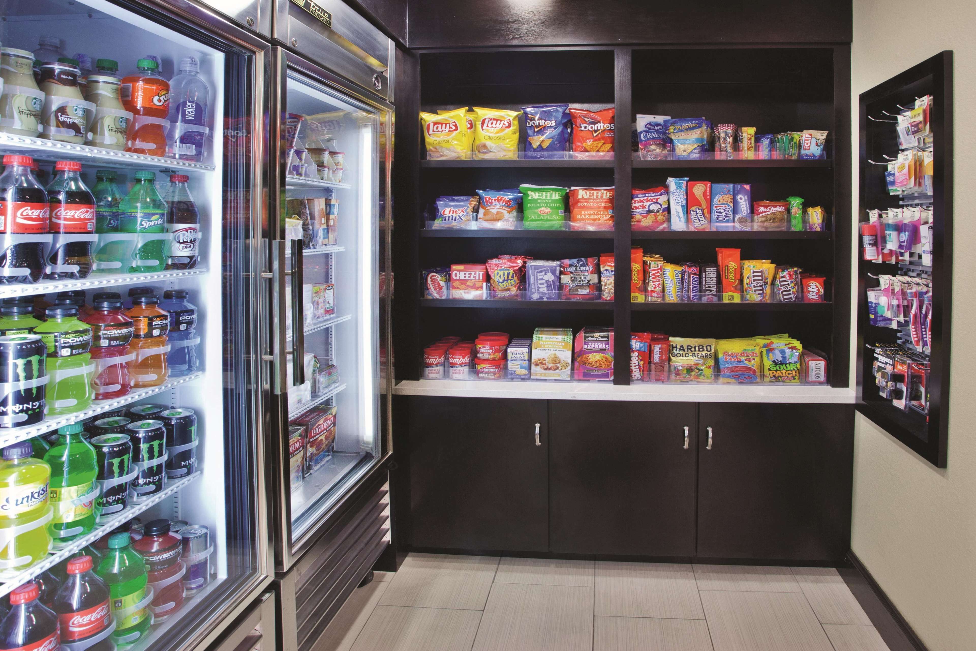 Mostrador refrigerado con diversas gaseosas y bebidas energéticas, junto a una estantería con papas fritas y aperitivos.
