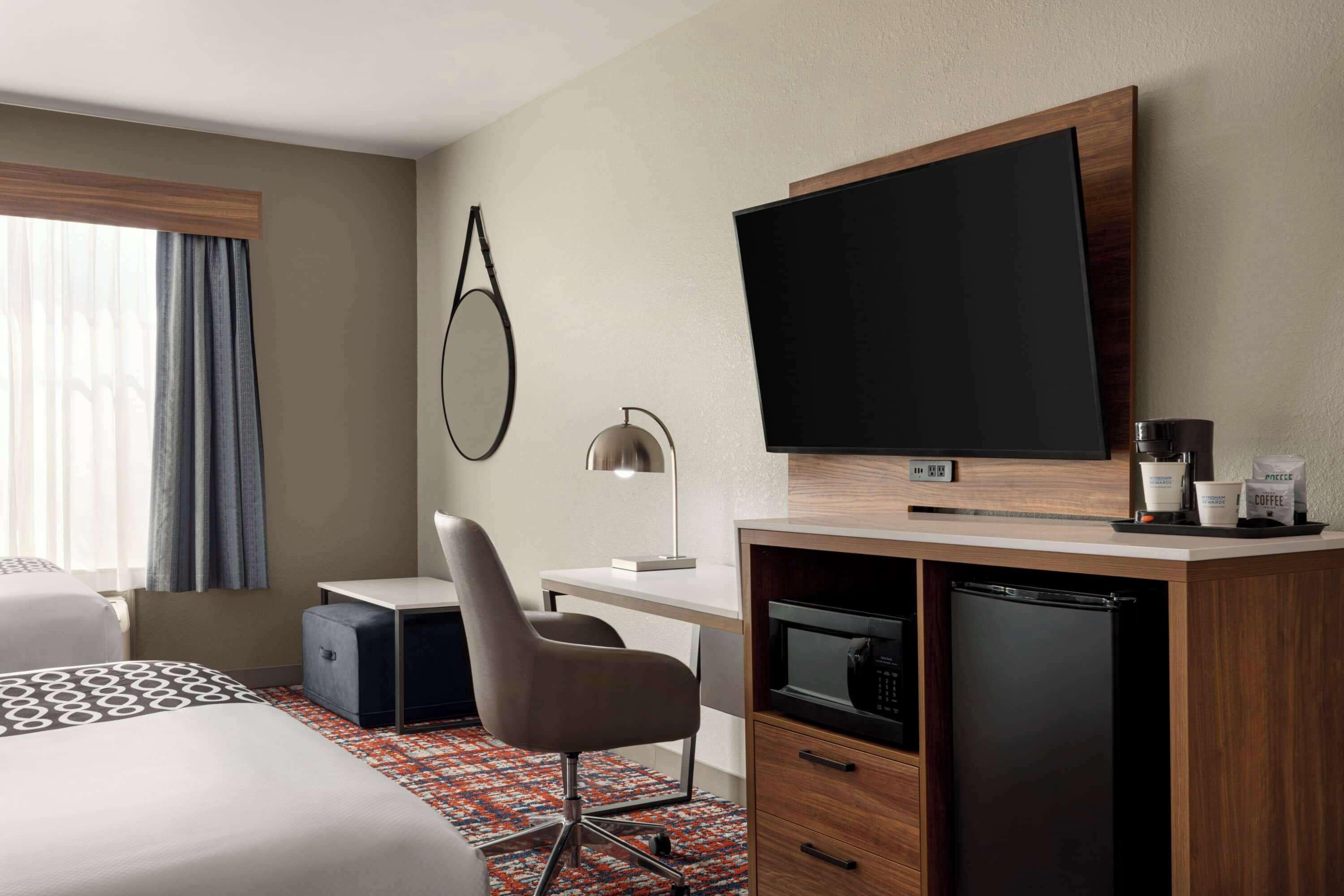 Una habitación de hotel con cama, escritorio, silla, televisor, cafetera y refrigerador.