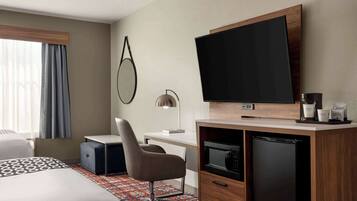Una habitación de hotel con cama, escritorio, silla, televisor, cafetera y refrigerador.