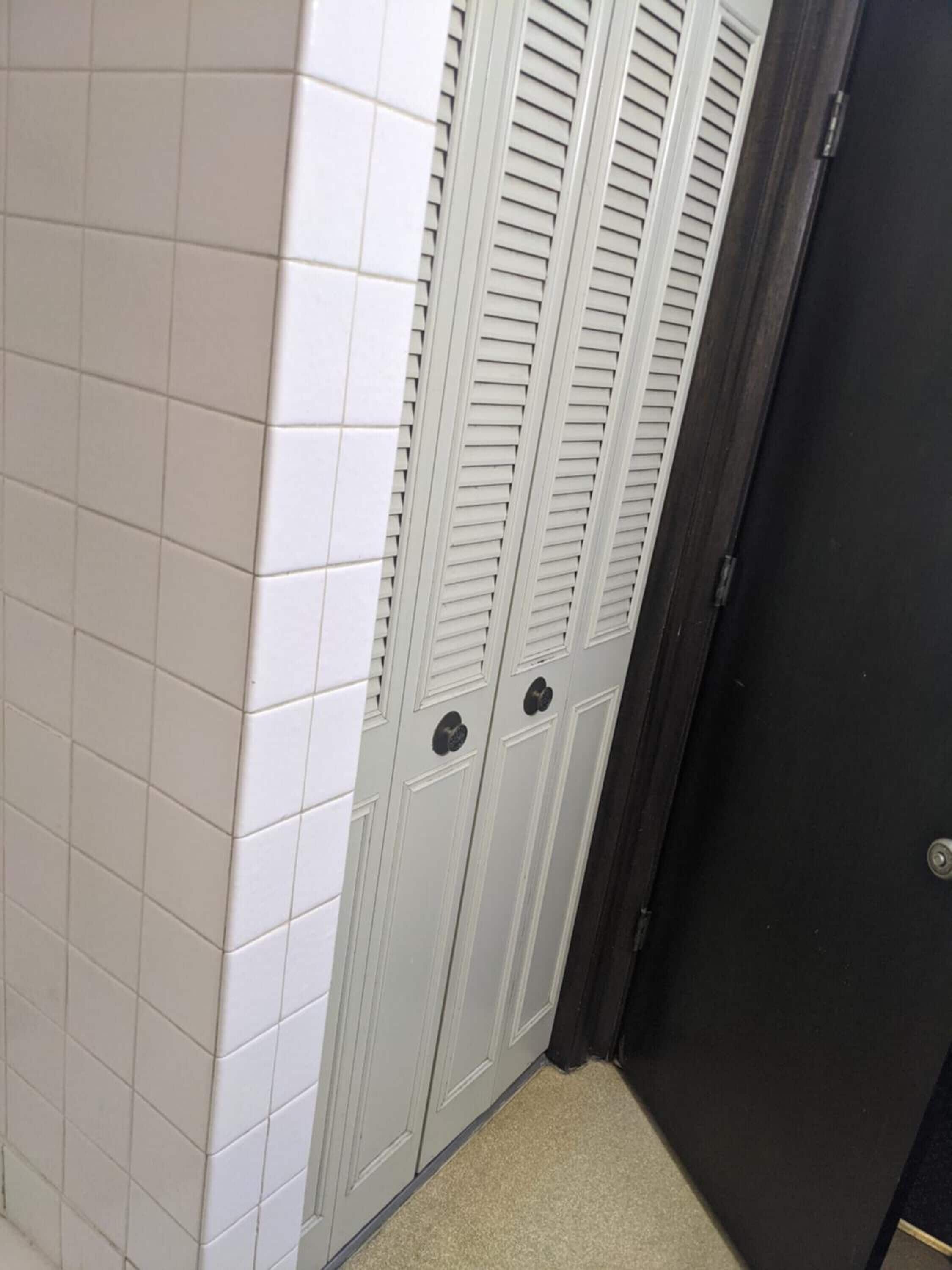 Um corredor com paredes de azulejos brancos e uma porta escura.