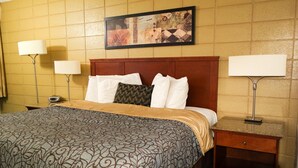 Ein Hotelzimmer mit einem großen Bett, zwei Nachttischlampen, einem hölzernen Kopfteil und einem gerahmten Kunstwerk an der Wand.