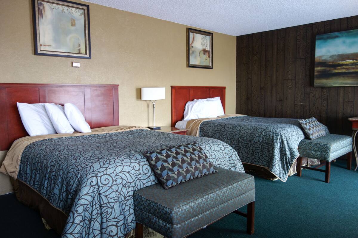 A hotel room with two beds, a bench, and a desk.