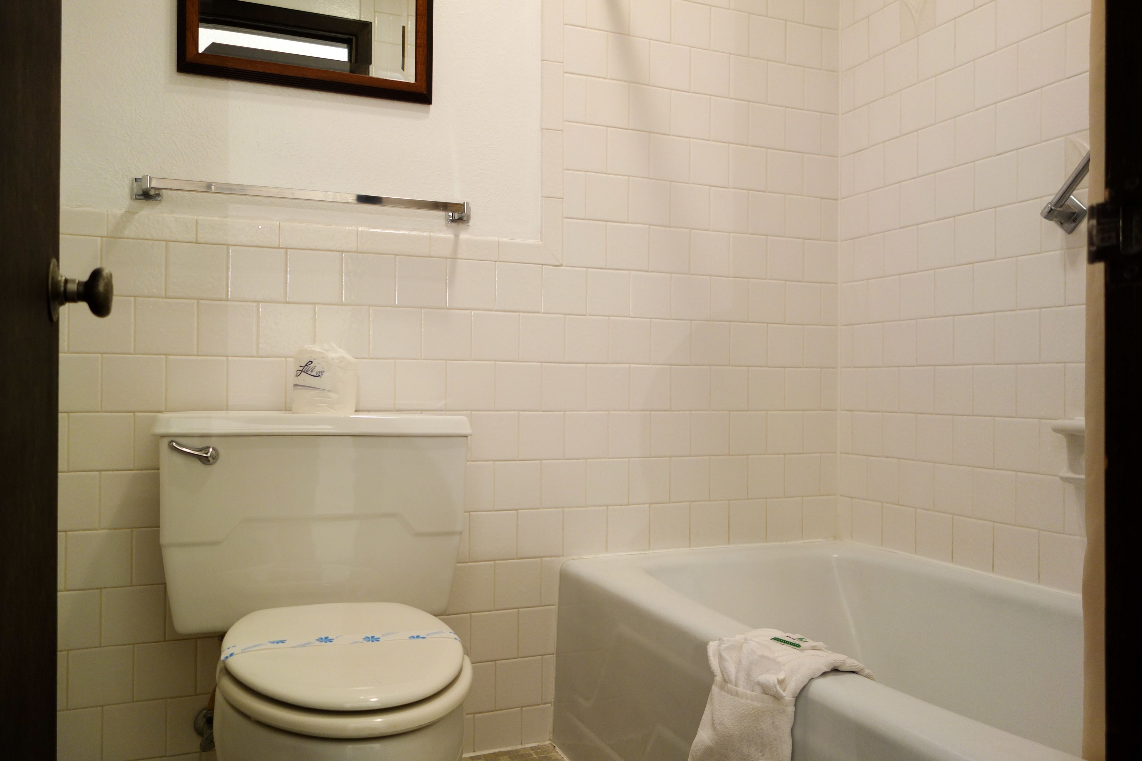 Un baño con inodoro, bañera y espejo sobre el inodoro.