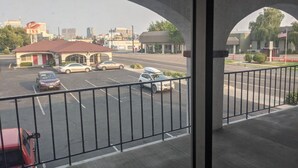 Blick vom Balkon auf einen Parkplatz mit mehreren Autos, ein Gebäude mit rotem Dach und eine Stadtlandschaft im Hintergrund.