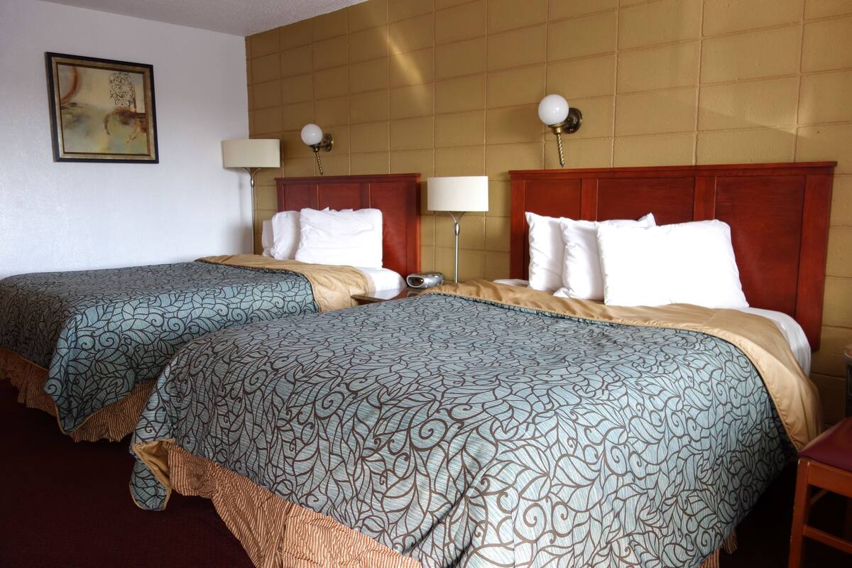 A hotel room with two beds, each with a patterned bedspread, a wooden headboard, bedside lamps, and a painting on the wall.