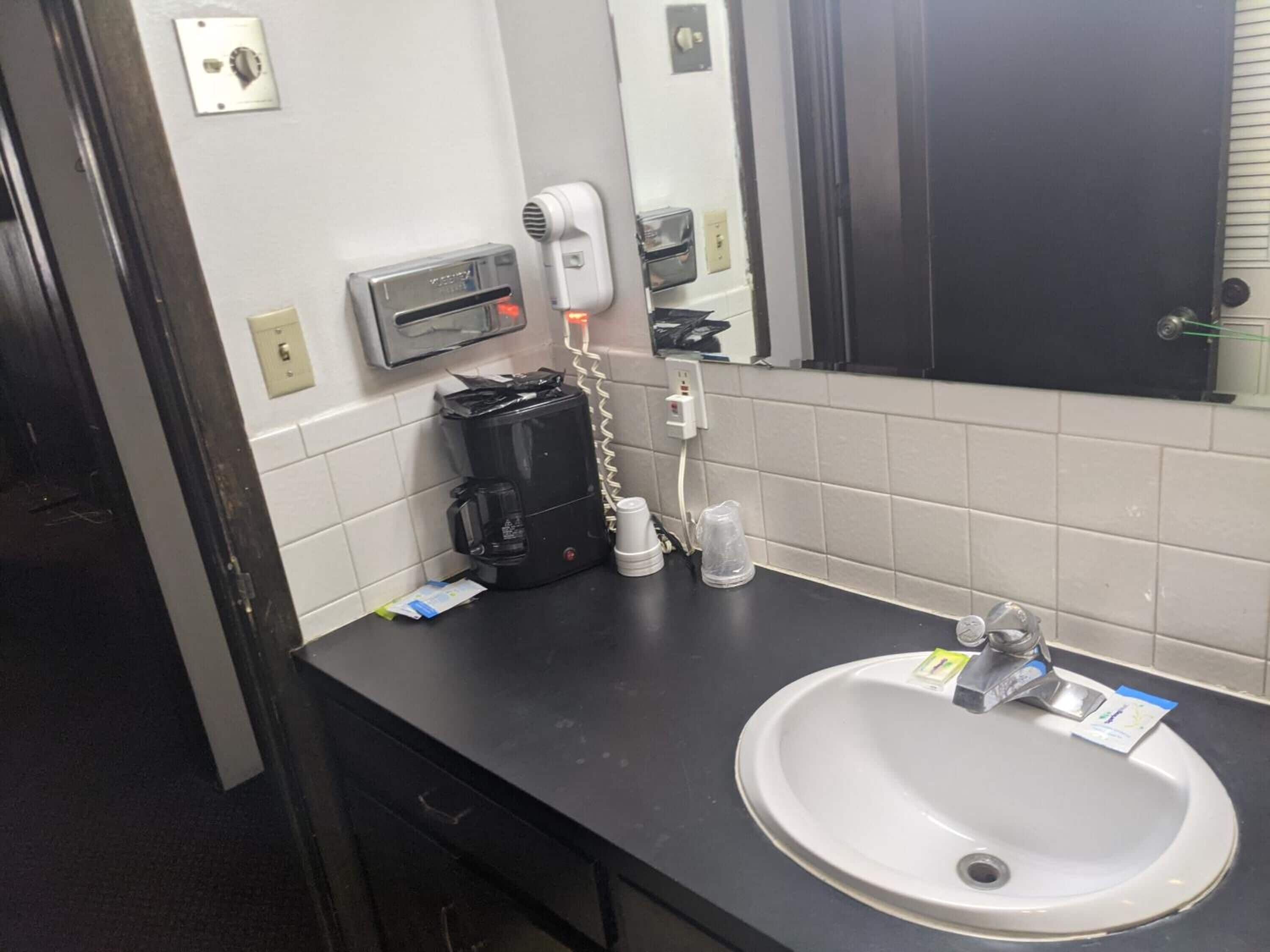 Ein Hotelbad mit Waschbecken, Spiegel und einer Kaffeemaschine auf der Ablagefläche.