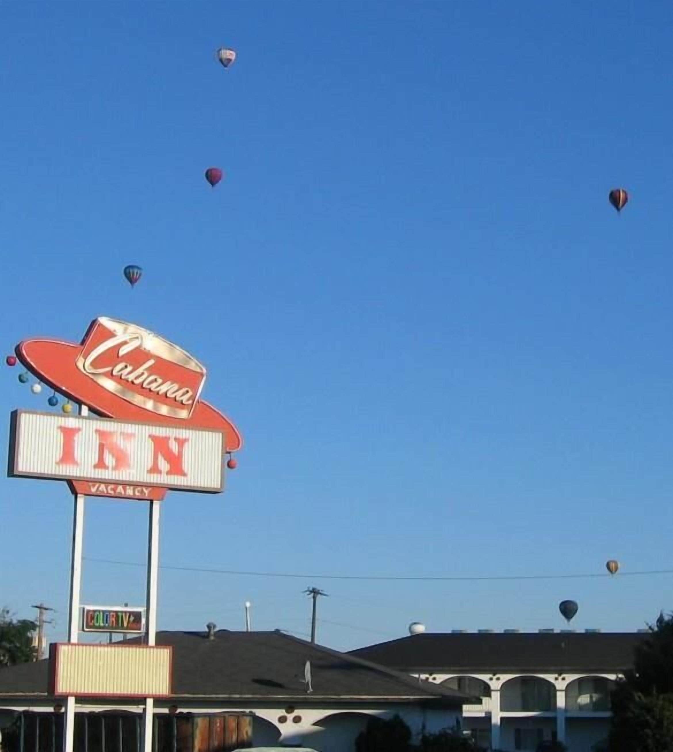 A hotel sign with 'Cabela's' and 'INN' branding, a 'VACANCY' sign below, and hot air balloons in the sky.