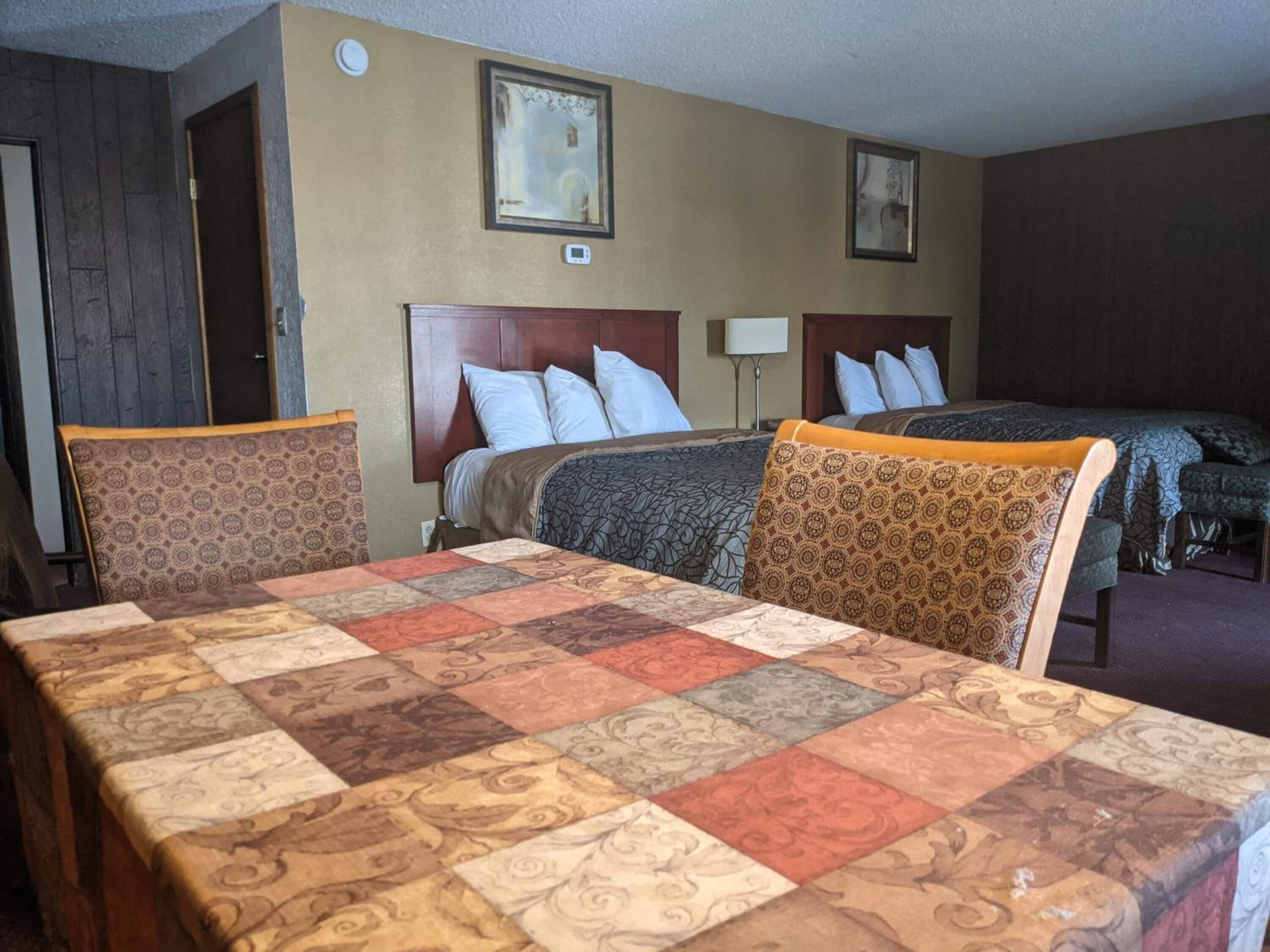 A hotel room with a large bed, two smaller beds, a desk, and two chairs.