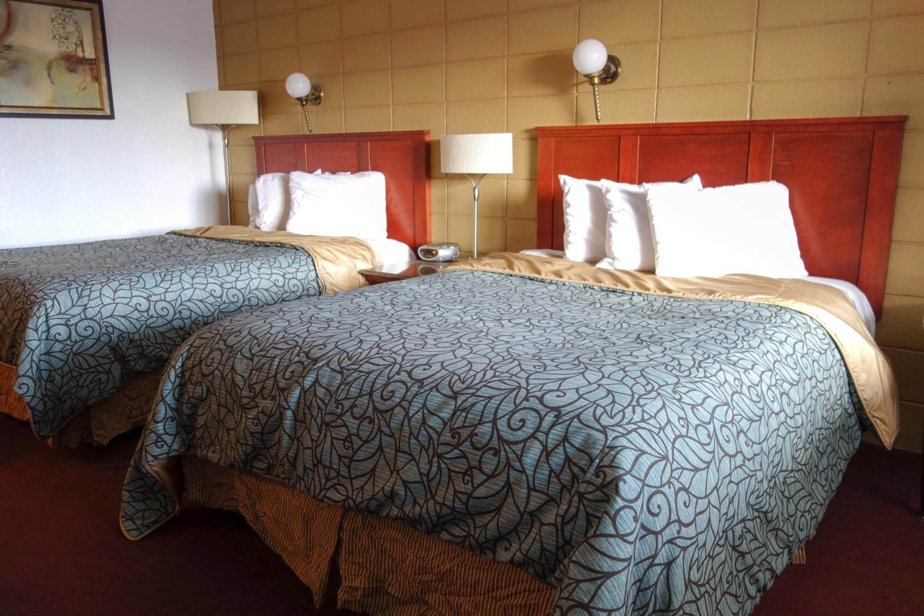 Two double beds with matching headboards and footboards, a bedside table with a lamp, and a wall-mounted artwork.