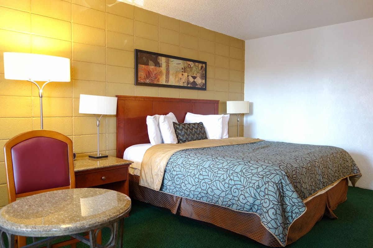 A hotel room with a bed, a chair, a table, and two lamps.