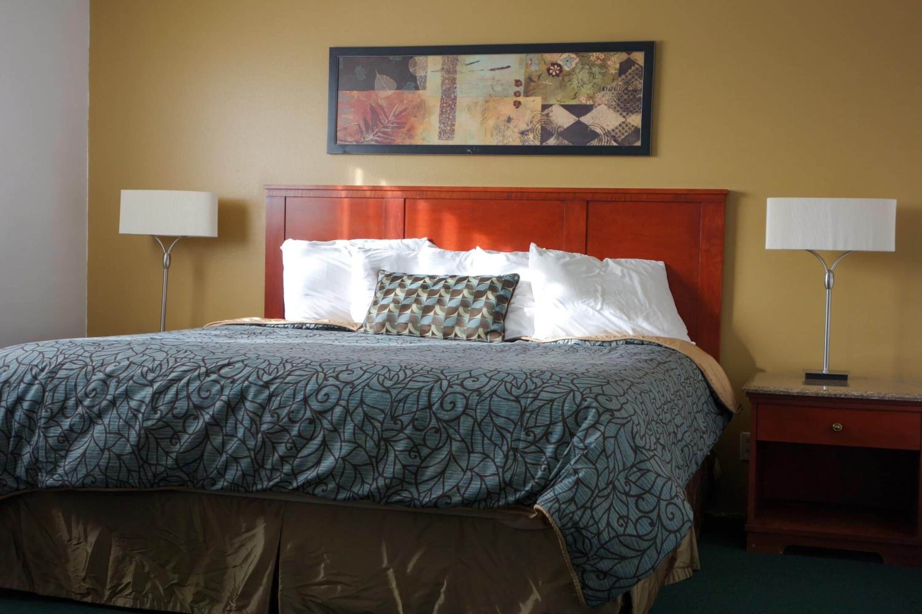 A hotel room with a large bed, two bedside lamps, a wooden headboard, and a framed artwork above the bed.