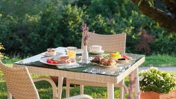 An outdoor dining table with wicker chairs, a glass table, and a view of a lush garden.