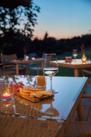 A table set for a meal with a glass of white wine, a candle, and a cheese board. - Hotel Relais Montemarino (Borgomale)