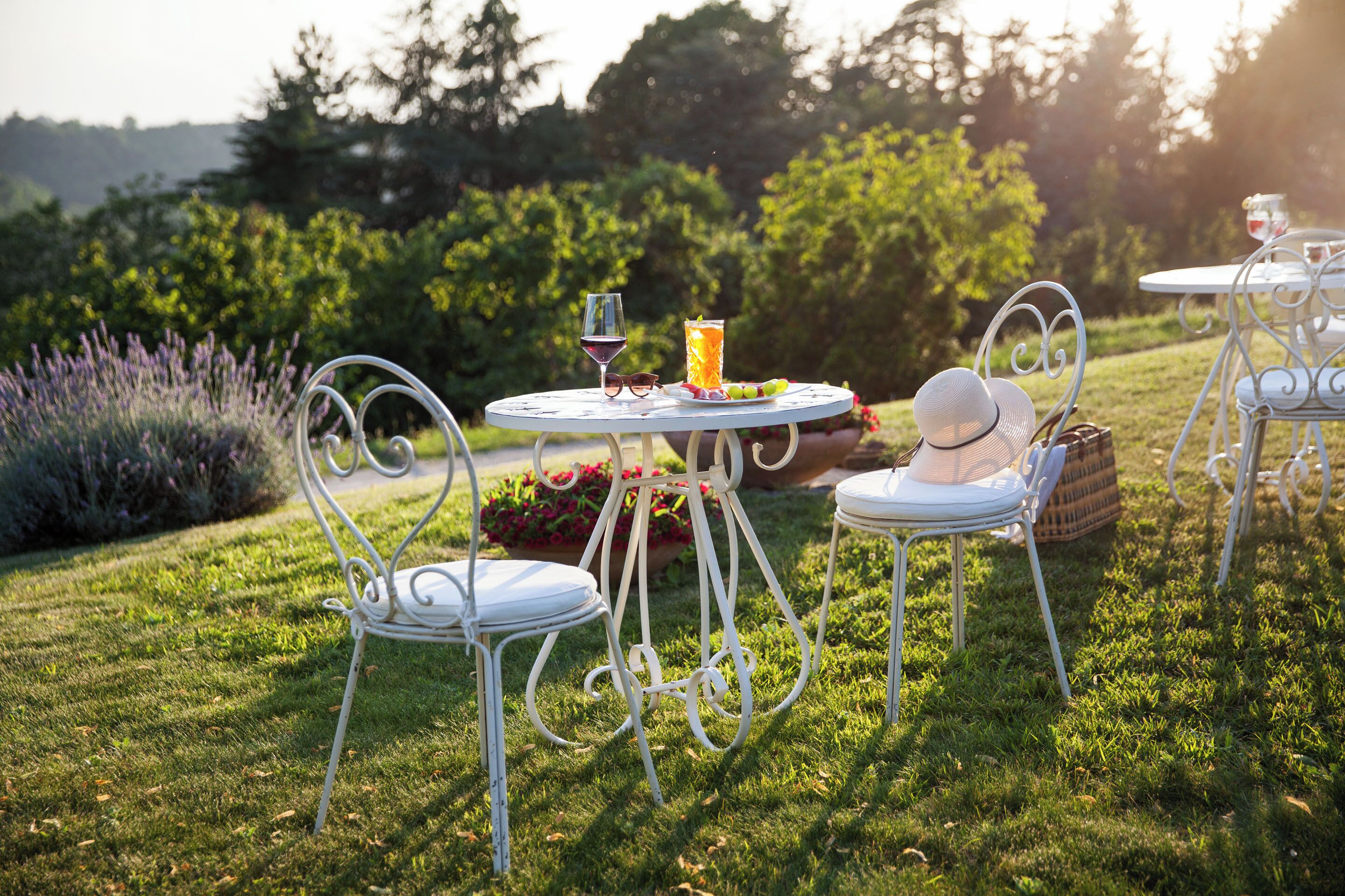 Un jardin agrémenté d’une table ronde et de chaises, un verre de vin rouge, un grand verre de jus d’orange et un panier de fruits.