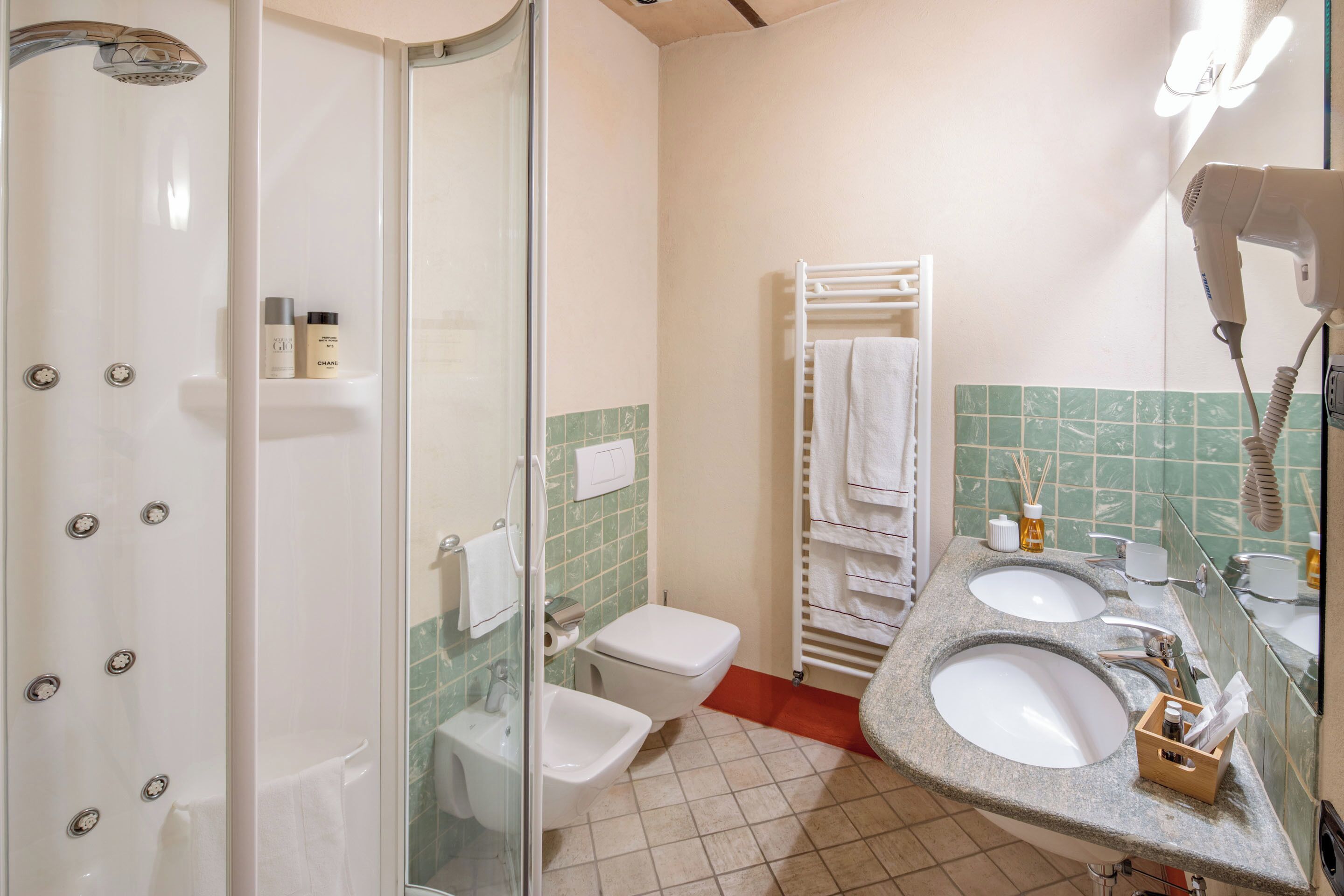 A bathroom with a glass shower enclosure, a toilet, a bidet, two sinks, a hairdryer, and a towel rack.