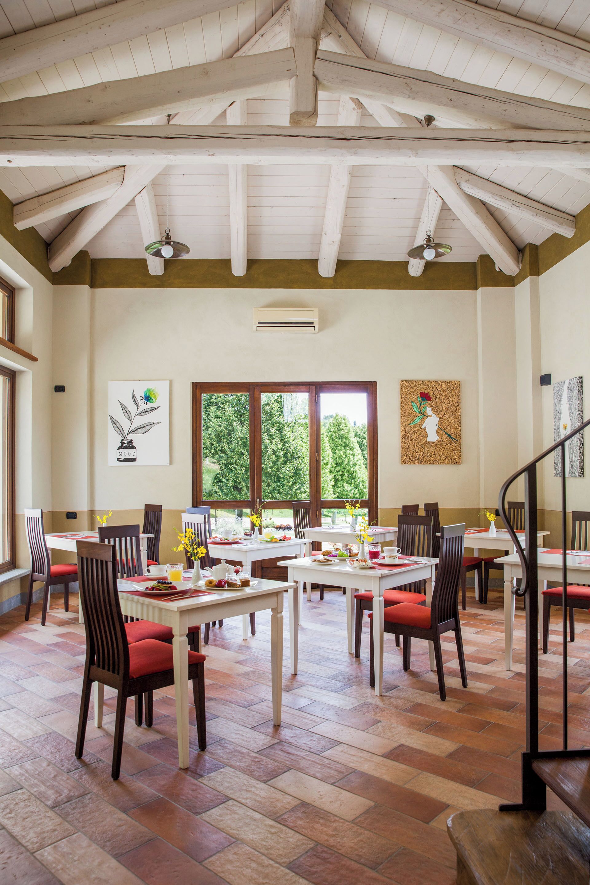 Un vaste espace dédié à la salle à manger, avec de nombreuses tables et chaises, de grandes fenêtres offrant une vue sur la verdure et une structure de plafond en bois.
