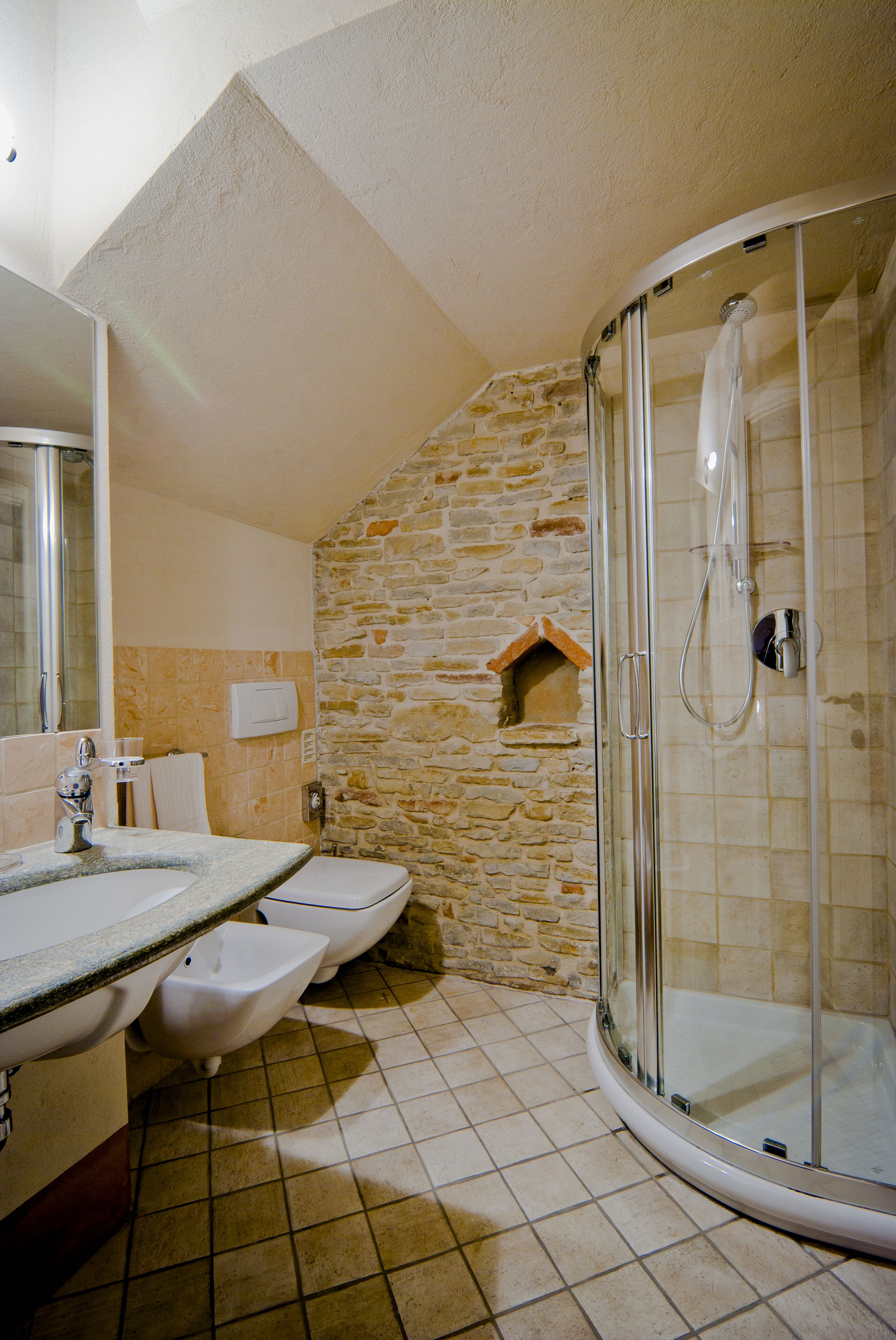 Un baño con pared de piedra, cabina de ducha de vidrio, lavamanos y retrete.