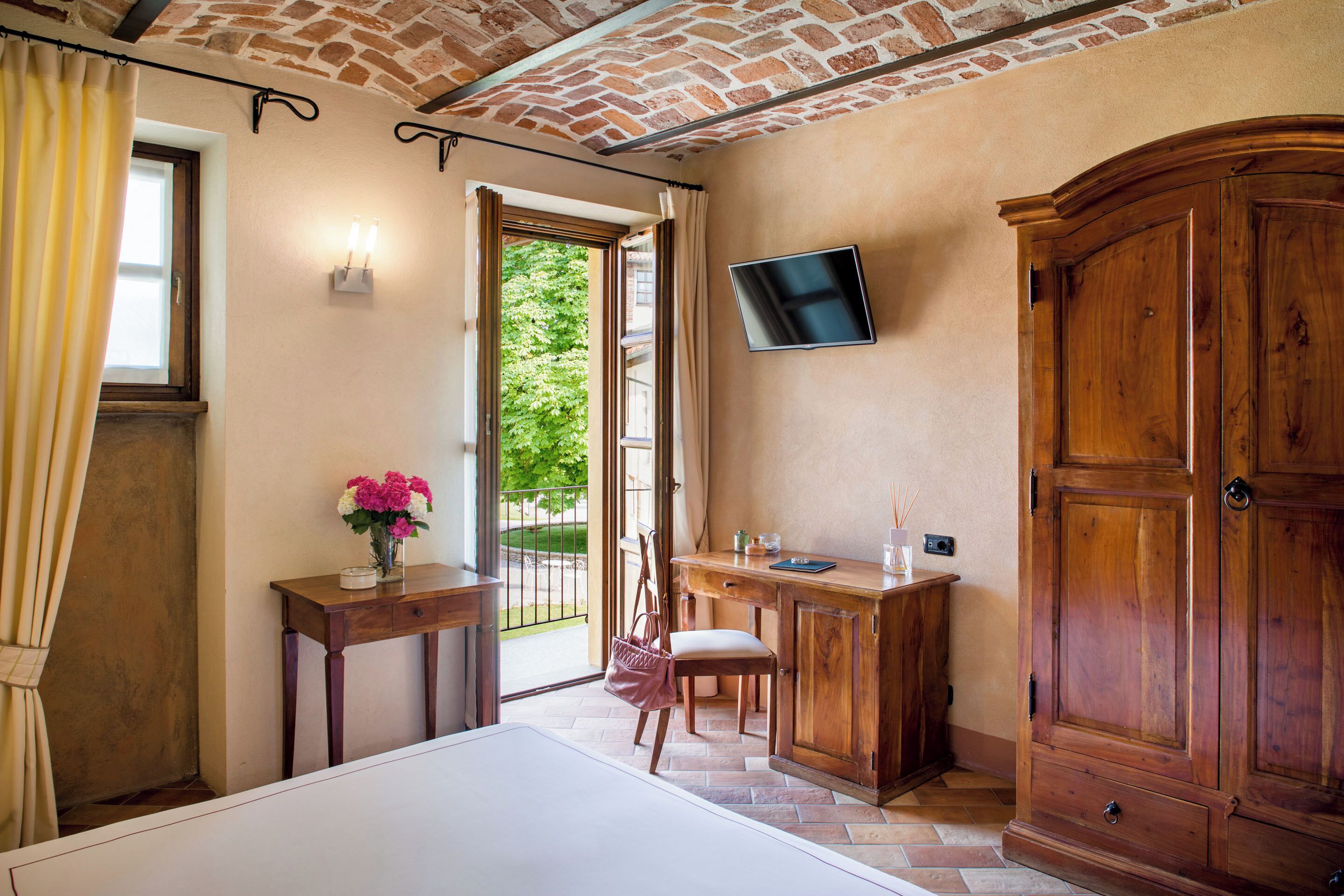 Una habitación con cama, un escritorio con silla, un televisor montado en la pared y un armario de madera grande.