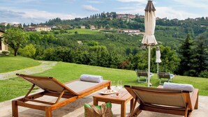 A patio with two wooden lounge chairs, a table, and a woven bag. - Hotel Relais Montemarino (Borgomale)