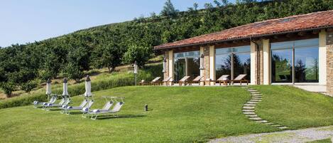 A building with a tiled roof, large windows, and a grassy lawn with sun loungers.