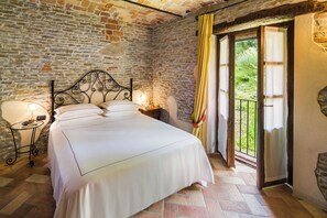 A bedroom with a stone wall, a bed with white linens, two bedside lamps, and a view through a glass door. - Hotel Relais Montemarino (Borgomale)
