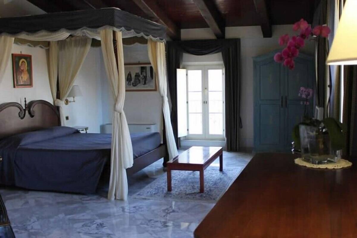 A bedroom with a four-poster bed, a bedside table, a nightstand, a lamp, and a window with curtains.