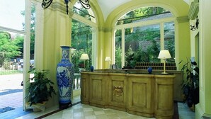 A reception area with a wooden counter, two lamps, and a large blue vase. - Hotel Roma Imperiale (Acqui Terme)