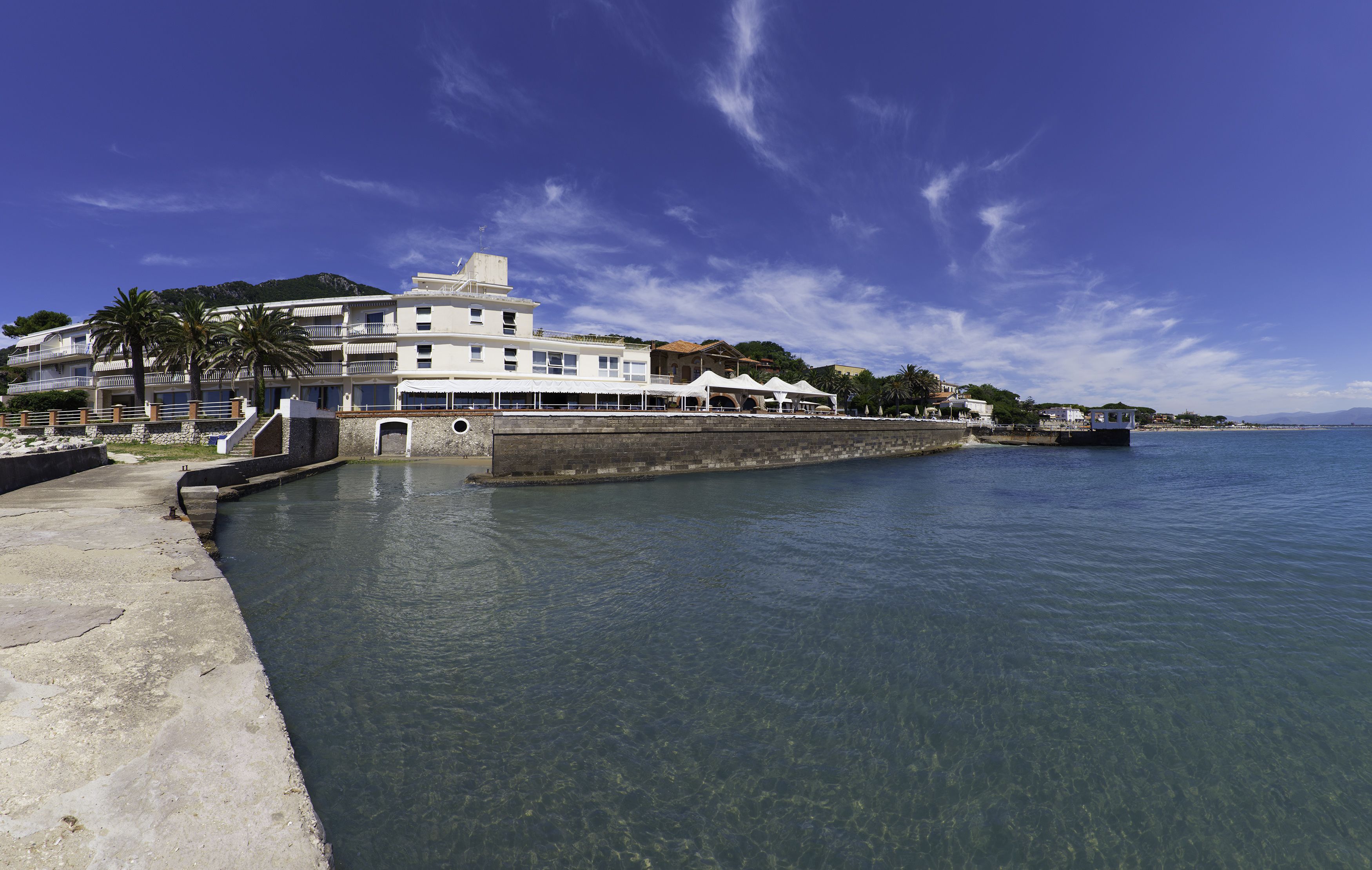 Un hotel frente al mar con vista despejada, un muelle de hormigón y un edificio con varios balcones.
