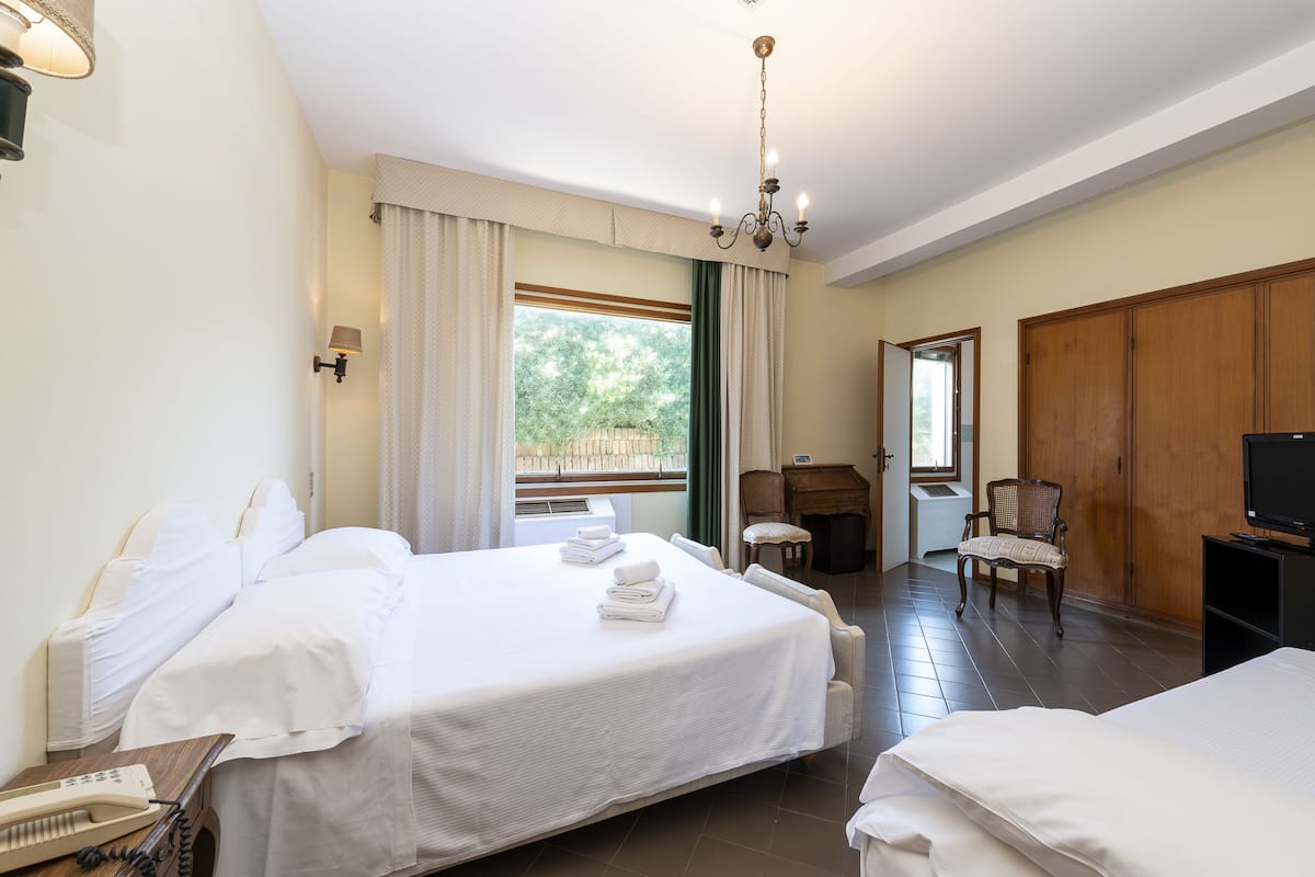 Ein Hotelzimmer mit zwei Betten, einem Schreibtisch, einem Sessel, einem Fernseher und einem Fenster mit Vorhängen.
