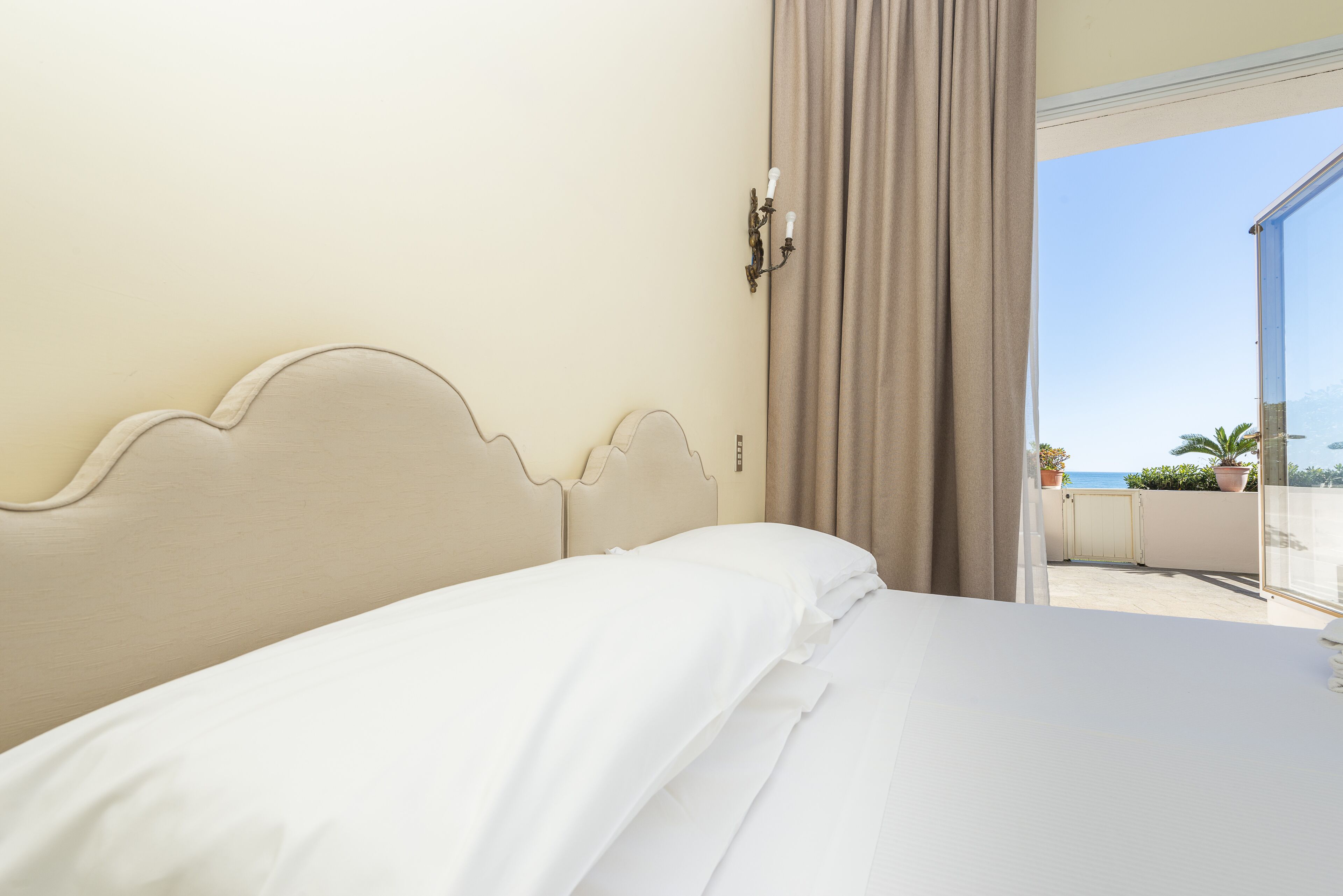 Una habitación de hotel con una cama, una ventana con cortinas y vistas al mar.