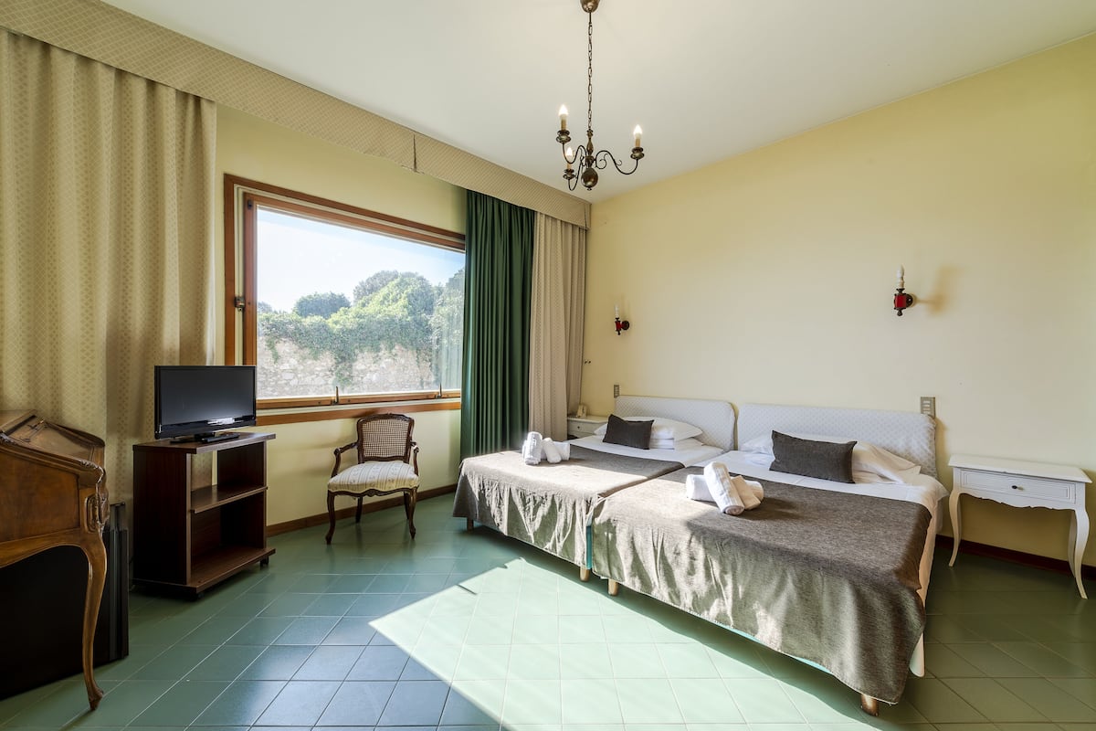 Ein Hotelzimmer mit Bett, Fernseher, Sessel, Schreibtisch und einem Fenster mit Vorhängen.