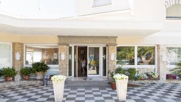 A hotel entrance with a checkered floor, stone facade, and potted plants.