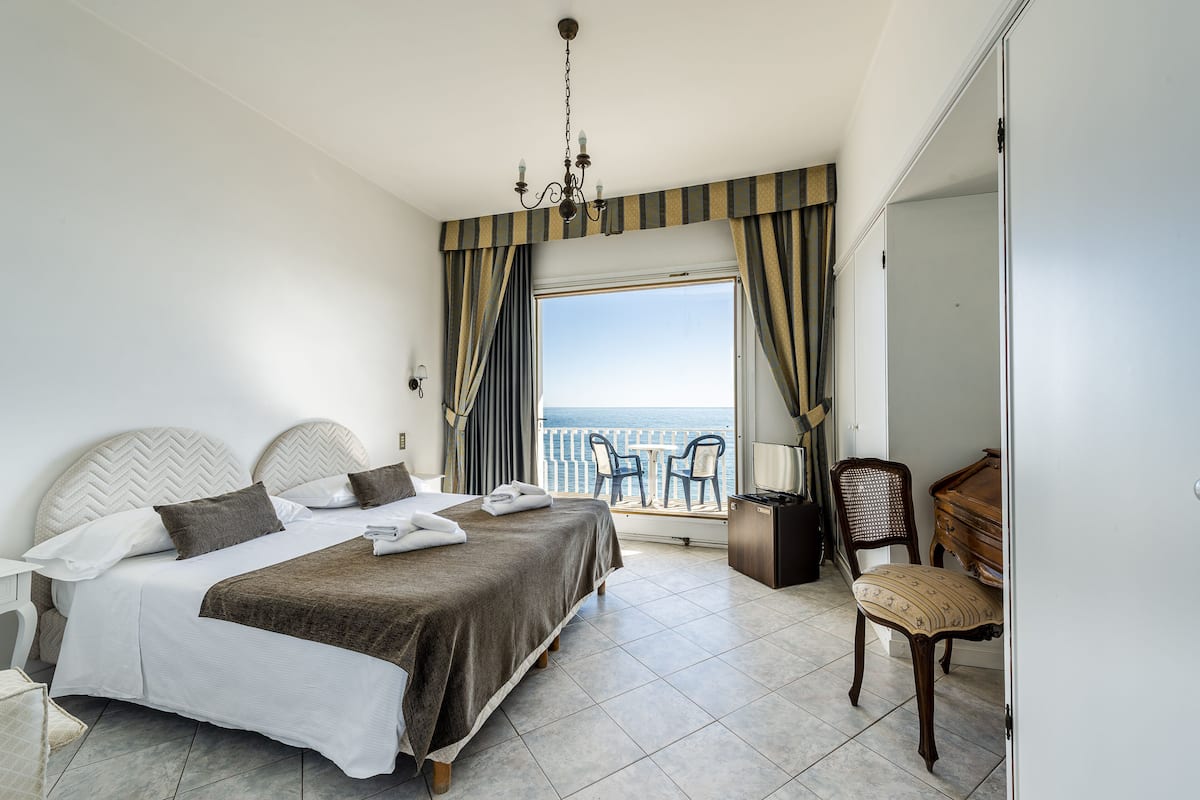 Ein Hotelzimmer mit Bett, Schreibtisch, Stuhl und Blick auf das Meer.