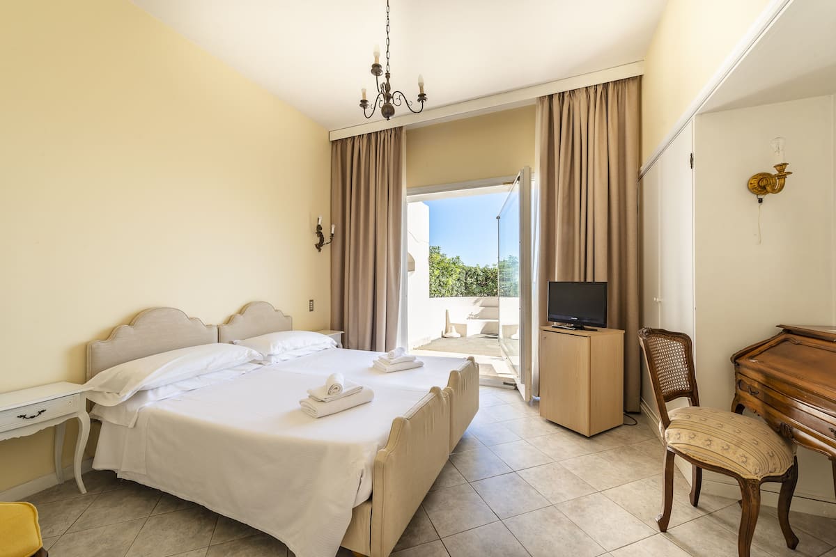 Ein Hotelzimmer mit Bett, Schreibtisch mit Fernseher, Stuhl und Blick ins Freie.
