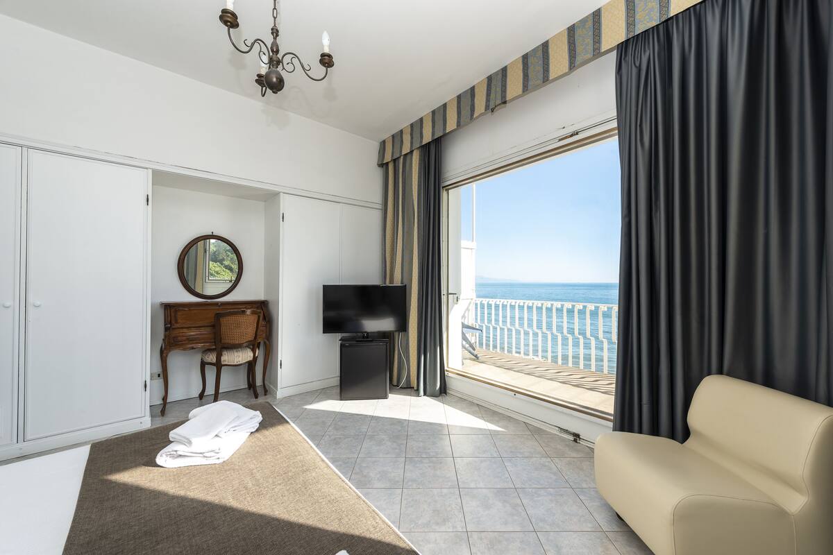 Ein Hotelzimmer mit großem Fenster, Flachbildfernseher, einer Couch, einem Schreibtisch mit Stuhl und einem Bett.