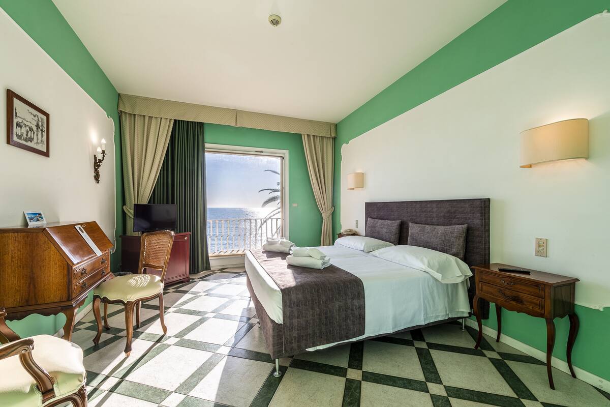 Ein Hotelzimmer mit Bett, Schreibtisch, Stuhl, Nachttisch und Meerblick.